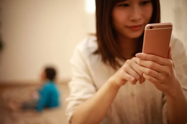 Giovane Madre Asiatica Utilizzando Smartphone Bambino Sullo Sfondo — Foto Stock
