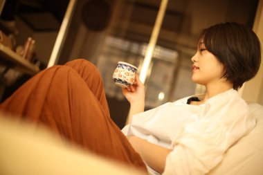 Genç Asyalı kadın evde çay içiyor.