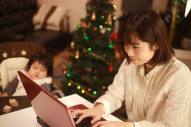 Küçük kızı sandalyede otururken genç anne dizüstü bilgisayar kullanıyor.