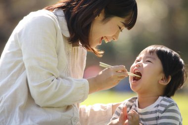 Asyalı anne oğluyla parkta yemek yiyor.