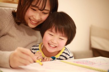 gülümseyen Asyalı genç kadın ve küçük oğlu resim çiziyor. 