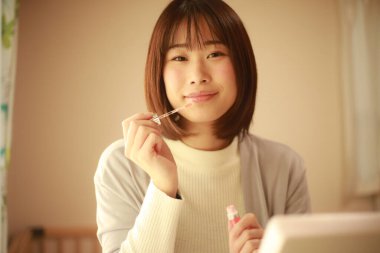 Genç Asyalı kadın makyaj yapıyor ve aynaya bakıyor.