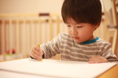 Küçük çocuk evdeki masaya resim çiziyor.