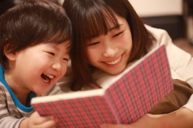 Mutlu Asyalı anne oğluna kitap okuyor.