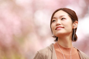 Kulaklıklı, bulanık bir arka planda müzik dinleyen Asyalı genç bir kadın.