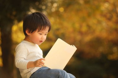 Parkta elinde kitapla yakışıklı bir oğlan.