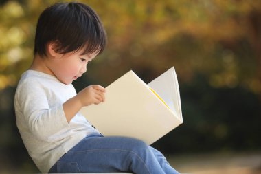 Parkta elinde kitapla yakışıklı bir oğlan.