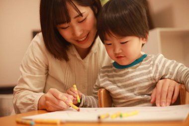 Beyaz kağıda boya kalemleri çizen genç anne ve oğul.