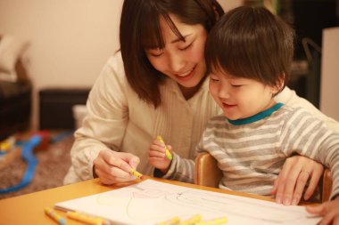Beyaz kağıda boya kalemleri çizen genç anne ve oğul.