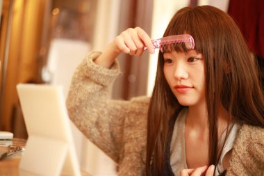 Güzel Asyalı genç kadın saçlarını tarıyor.