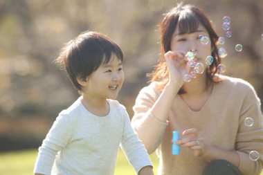 Asyalı anne ve küçük oğlu sabun köpüğü üflüyorlar.