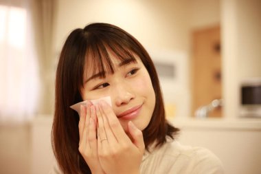 Genç Asyalı kadın makyaj yapıyor ve aynaya bakıyor.