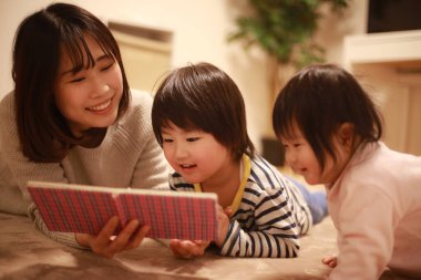 Mutlu genç anne çocuklarla kitap okuyor.