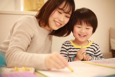 gülümseyen Asyalı genç kadın ve küçük oğlu resim çiziyor. 