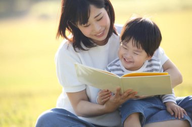 Mutlu Asyalı anne oğlu için kitap okuyor.