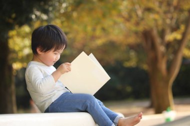 Parkta elinde kitapla yakışıklı bir oğlan.