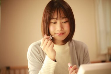 Genç Asyalı kadın makyaj yapıyor ve aynaya bakıyor.