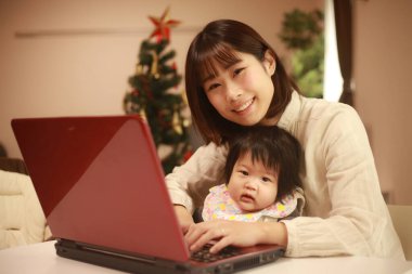 Küçük kızıyla birlikte dizüstü bilgisayar kullanan mutlu Japon kadın.