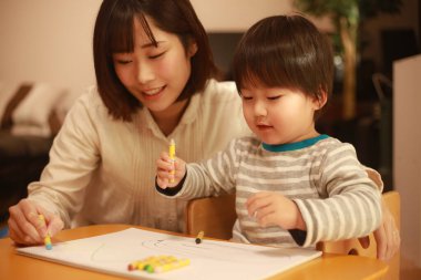 Beyaz kağıda boya kalemleri çizen genç anne ve oğul.