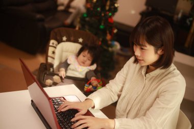 Küçük kızı sandalyede otururken genç anne dizüstü bilgisayar kullanıyor.