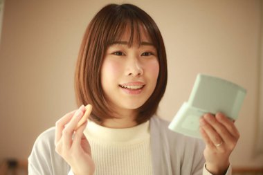 Genç Asyalı kadın makyaj yapıyor ve aynaya bakıyor.