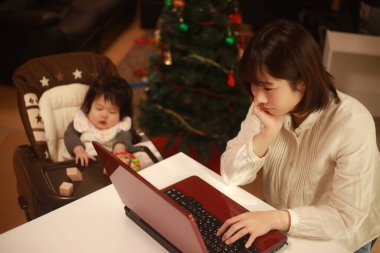 Küçük kızı sandalyede otururken genç anne dizüstü bilgisayar kullanıyor.