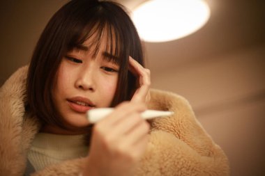 Asyalı kadın vücut ısısını dijital termometreyle kontrol ediyor