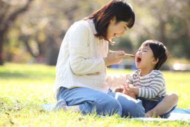 Asyalı anne oğluyla parkta yemek yiyor.
