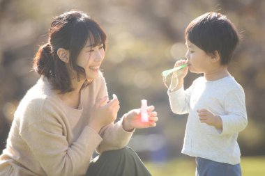 Asyalı anne ve küçük oğlu sabun köpüğü üflüyorlar.