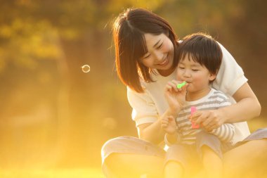 Asyalı anne ve küçük oğlu sabun köpüğü üflüyorlar.