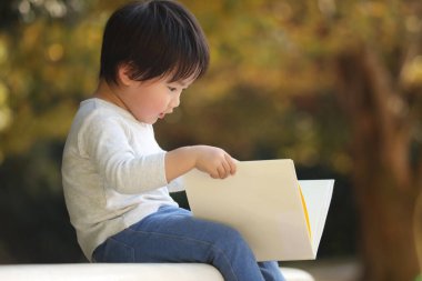 Parkta elinde kitapla yakışıklı bir oğlan.