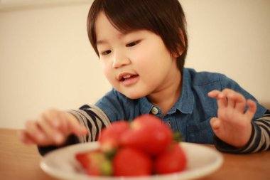 Küçük çocuk mutfakta çilek yiyor. 