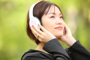 Parkta kulaklıklı Asyalı genç bir kadının portresi. 