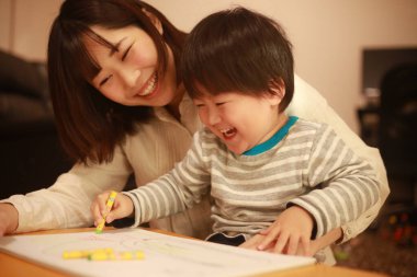 Beyaz kağıda boya kalemleri çizen genç anne ve oğul.