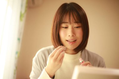 Genç Asyalı kadın makyaj yapıyor ve aynaya bakıyor.