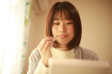 Genç Asyalı kadın makyaj yapıyor ve aynaya bakıyor.