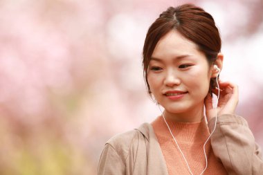 Genç Asyalı kadın sokakta kulaklıkla müzik dinliyor.