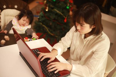 Küçük kızı sandalyede otururken genç anne dizüstü bilgisayar kullanıyor.