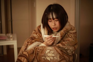 Asyalı kadın vücut ısısını dijital termometreyle kontrol ediyor