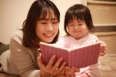 Mutlu genç anne çocuklarla kitap okuyor.