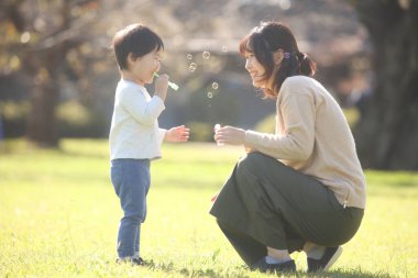 Asyalı anne ve küçük oğlu sabun köpüğü üflüyorlar.