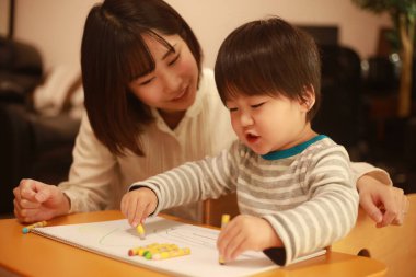 Beyaz kağıda boya kalemleri çizen genç anne ve oğul.