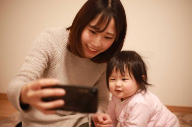 Anne ve kızı cep telefonuyla selfie çekiyorlar.