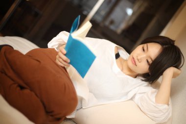 Kanepede kitap okuyan güzel bir kadın.