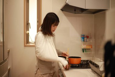 Kırık kollu Asyalı genç kadın mutfakta yemek pişiriyor.