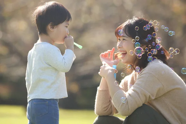 Asyalı anne ve küçük oğlu sabun köpüğü üflüyorlar.
