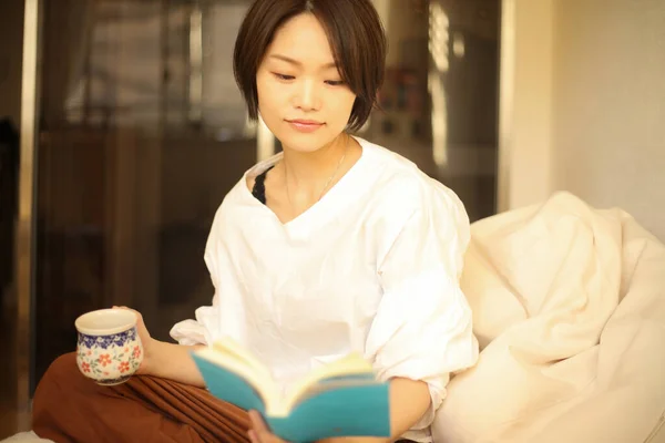 美丽的女人躺在沙发上看书 — 图库照片