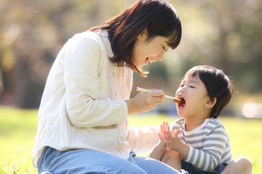 Asyalı anne oğluyla parkta yemek yiyor.