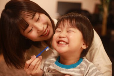 Genç anne, küçük oğlu için dişlerini fırçalıyor.