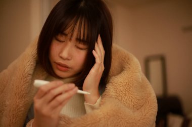 Asyalı kadın vücut ısısını dijital termometreyle kontrol ediyor